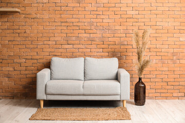 Comfortable sofa and vase with pampas grass near brick wall