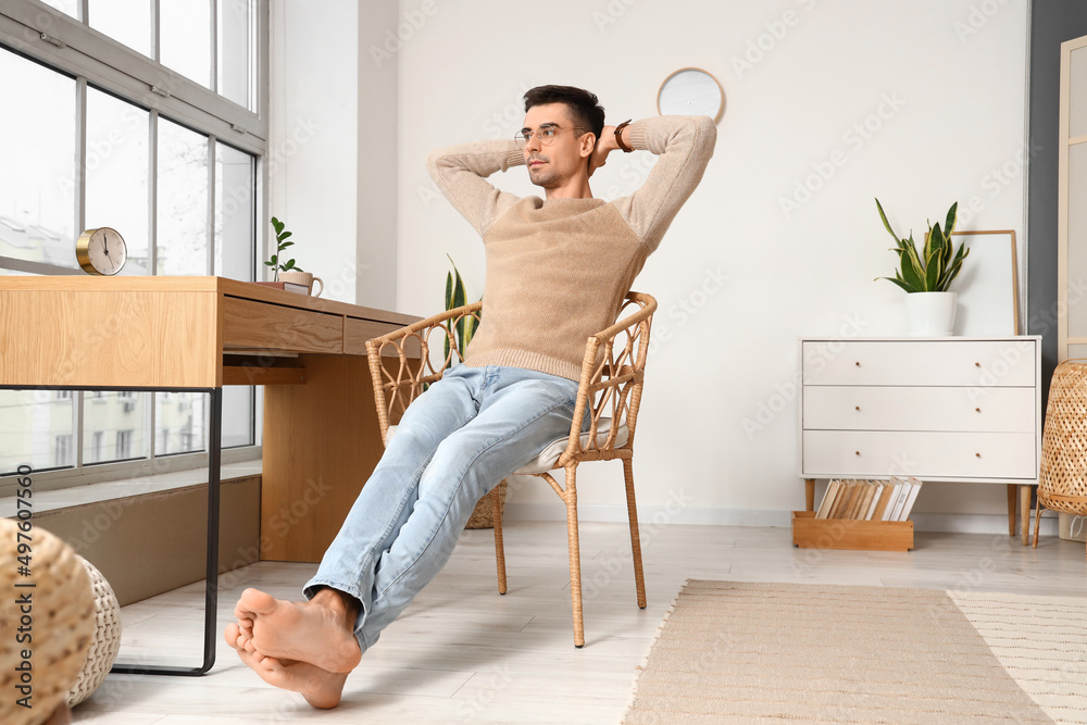 Poster young barefooted man relaxing in armchair at home