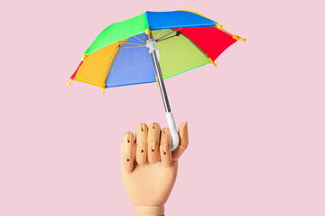 Wooden hand with open umbrella on pink background