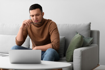 Worried young man with eyeglasses sitting on sofa at home