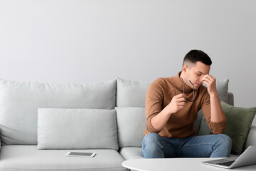 Worried young man with eyeglasses sitting on sofa at home