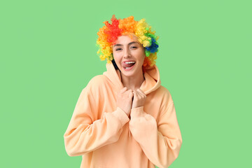 Funny young woman in colorful wig on green background. April fools' day celebration