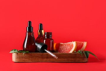 Wooden board with bottles of grapefruit essential oil on red background