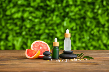 Composition with bottles of grapefruit essential oil and spa stones on wooden table outdoors