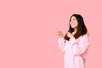 Obraz na płótnie Canvas Young Asian woman in hoodie pointing at something on pink background