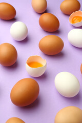 Cracked and whole chicken eggs on purple background