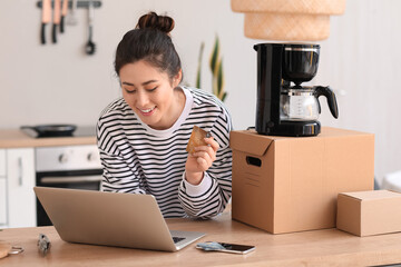 Young woman with laptop, credit card and new coffee maker at home. Online shopping