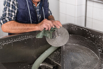 old hands of an elderly person scrubbing a metal filter used in the manufacture of fresh cheeses