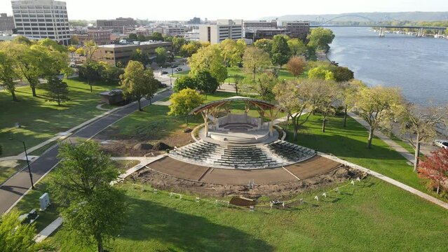 Pan out over park along the Mississippi River in summer. Construction continuing on bandshell area. Bridges over the Mississippi River. Cityscape in the background. Bright summer day. 