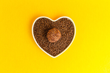 Brigadeiro over a heart-shaped bowl on a yellow background. I love brigadier.