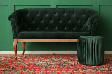Sofa with pouf and vintage carpet near green wall