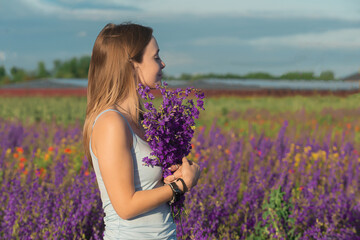 a beautiful girl with blond hair holds a bouquet of field bright lilac flowers in her hands