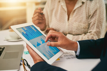 Taking a closer look at the latest business stats. Closeup shot of two unrecognisable businesspeople analysing graphs on a digital tablet in an office.