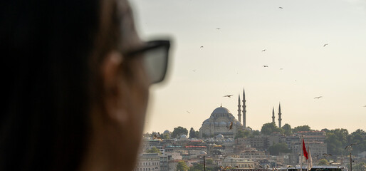 Fototapeta na wymiar Woman with sunglasses observing the views of the Bosphorus River and the Suleiman Mosque from the Galata Bridge