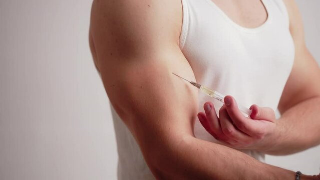 Studio shot of bodybuilding cheater using doping by injection to his biceps muscle. Studio shot over white background. High quality 4k footage