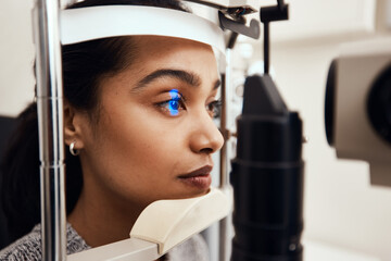 Keep as still as possible. Shot of a young woman getting her eyes examined with a slit lamp.