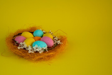 Happy Easter! Easter card with a picture of a nest of colored eggs on a yellow background decorated with flowers