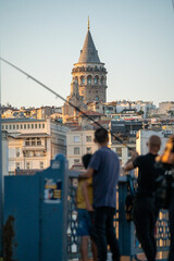 Fototapeta na wymiar Fishermen with fishing rods on the Galata Bridge overlooking the Galata Tower in Istanbul, Turkey