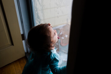 toddler girl licks window glass