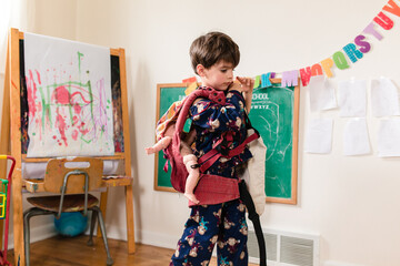 boy wears toy baby doll in baby carrier