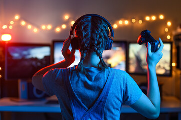 Gaming and e-sports. Girl gamer, streamer playing games using the joystick and gamepad. On three monitors, Creative light © Anton