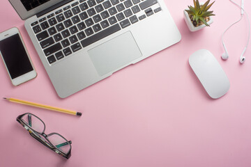 Pink office desk with an empty laptop, computer keyboard and other stationery. Top view with copy space, flat lying.