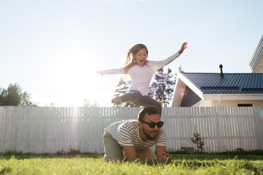 Excited Child Jumping Over Dad In Backyard