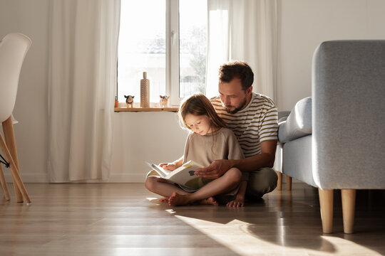 Father and daughter reading book on floor