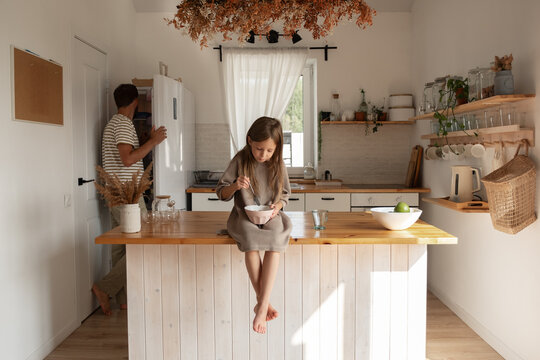 Daughter having breakfast near cooking father