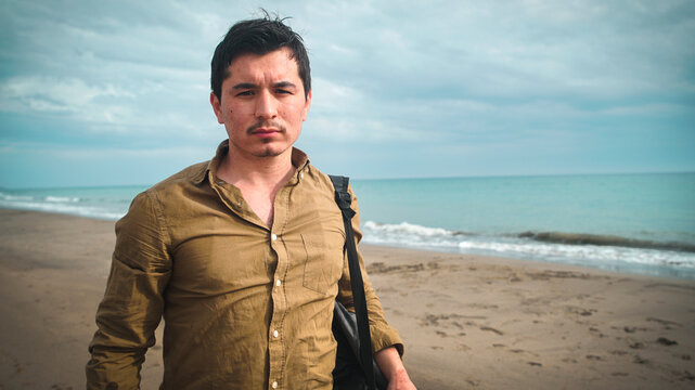 Young adult on a beach looking thoughtfully to the camera with sea on background