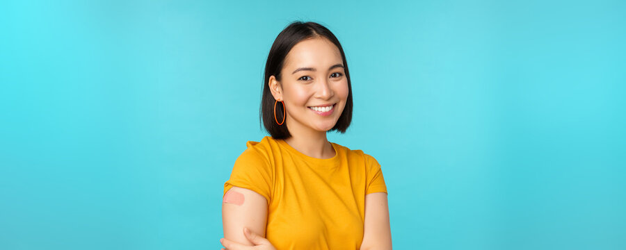 Vaccine campaign from covid-19. Young beautiful, healthy asian woman showing shoulder with bandaid, concept of vaccination, standing over blue background