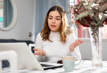 Smiling young female using computer for distance video communication with coworkers from home