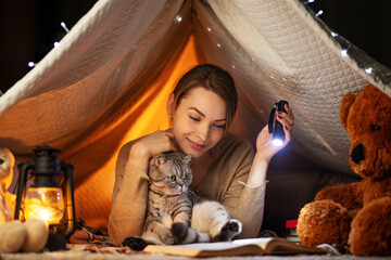 Before bedtime. A girl with a Scottish and British cat reading a book in a tent. A concept of rest, fairy tales, night, sleep and warmth, dreams