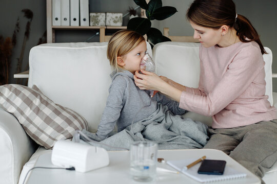 Woman doing inhalation to sick child sitting on sofa