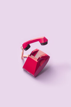 Red stationary dial phone over pink background