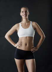 Fototapeta na wymiar I work hard to look this good. Studio portrait of a sporty young woman standing against a dark background.