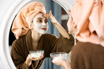 Happy woman taking care of face skin with the lotion