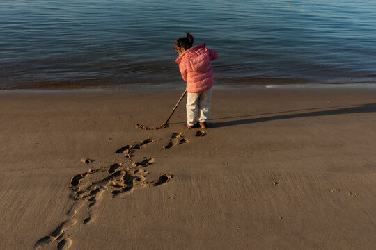 Kid drawing with stick on seashore during winter