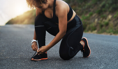 Lace up so you dont trip over your goals. Shot of a sporty young woman tying her laces while exercising outdoors.