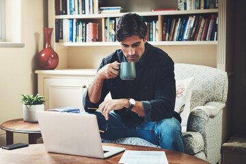 Its all in a days work. Shot of a handsome young businessman drinking coffee while working on a laptop in his home office.