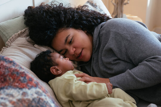 Smiling black mother caressing baby on bed