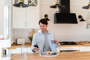 Portrait of happy man having breakfast and using phone