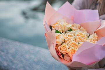 hand holding a flower. hands holding a rose. Present with beautiful bouquet of roses. bunch of flowers. Bunch of orange roses with pink papper and green leaves. Seaside background. Wedding bunch rose.