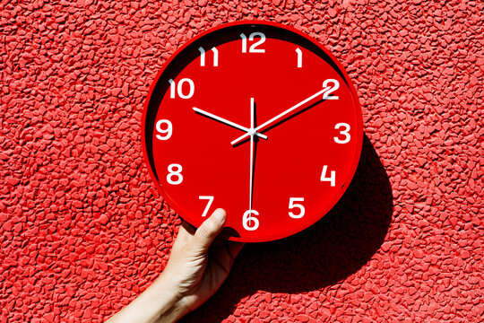 man holding a red clock in front of a red wall