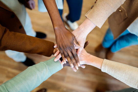 Crop diverse coworkers stacking hands in office
