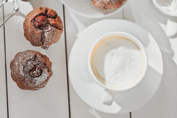 top view of homemade chocolate muffins with berry filling and a cup of coffee on wooden table. home baking, tasty breakfast for weekend.