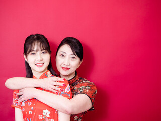 Portrait of a daughter and mother wearing traditional cheongsam qipao and smiling cuddling isolated on red background.