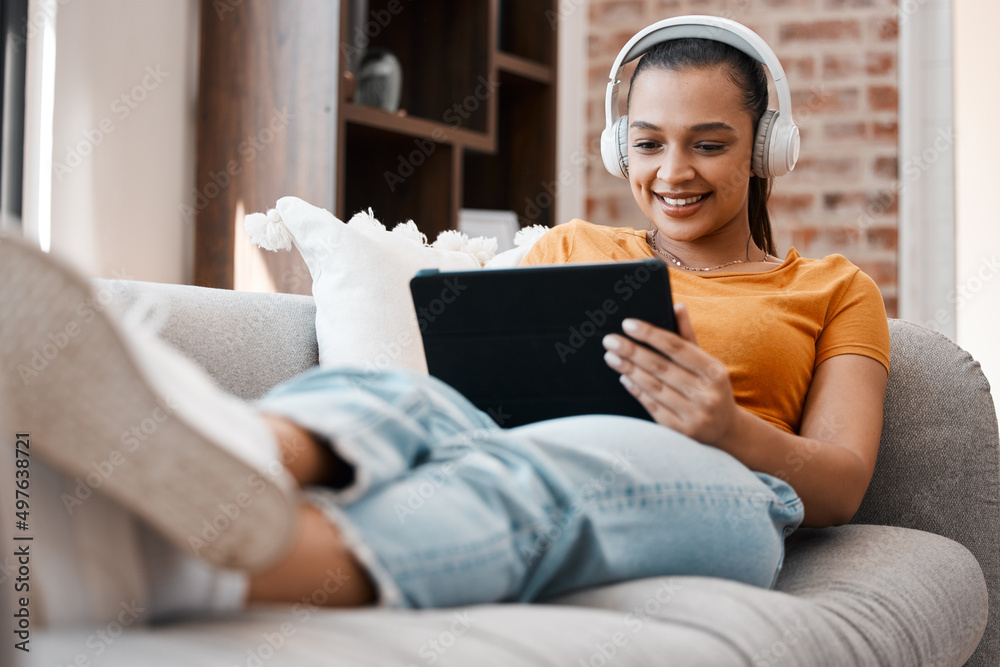 Poster catching up on my favourite show. shot of a young woman relaxing while using a digital tablet at hom
