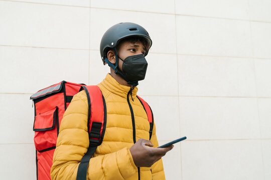 Young delivery man browsing mobile phone against wall