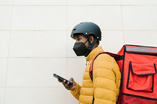 Male courier with smartphone working during epidemic
